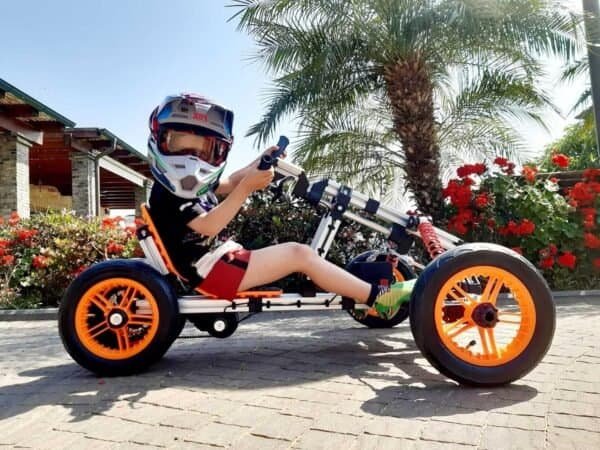 Child riding a pedal-powered tricycle with helmet outdoors.