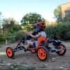 Child riding a go-kart with safety helmet outdoors.