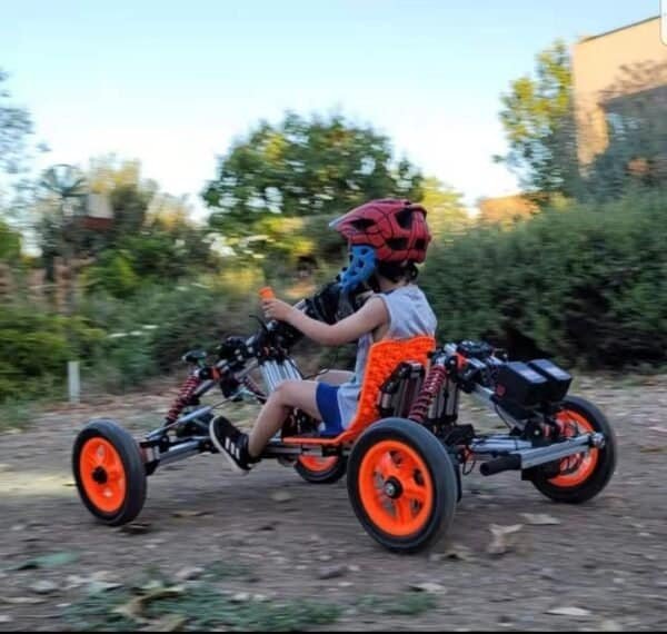Child riding a go-kart with safety helmet outdoors.